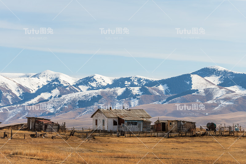 在群山的背景下，草原上一幢破败的乡村房屋和附属建筑