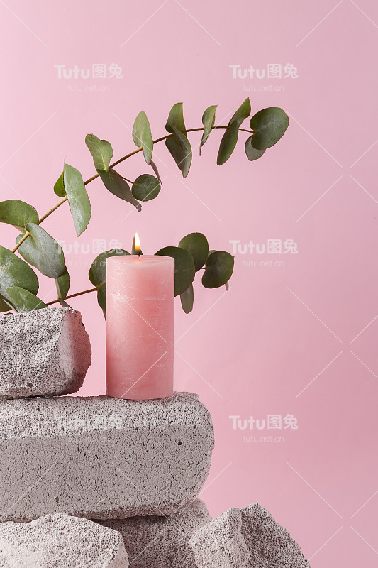 粉色燃烧的蜡烛在石头与桉树树枝。水疗，美容理念。现代静物产品照片。唯美的极简主义构图。