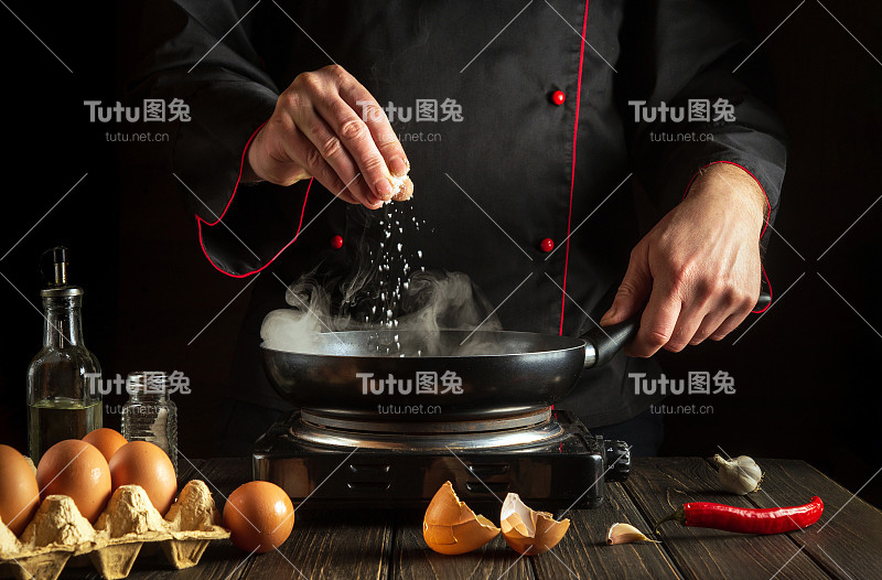 厨师在锅里煮鸡蛋时加盐。厨房餐桌上的工作环境。餐厅或酒店的菜单创意。