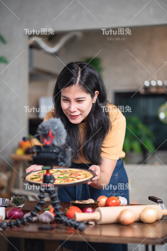 美丽的亚洲女人穿着围裙准备在网上课堂上直播，在家里厨房制作fods。小型商业餐厅和美食。