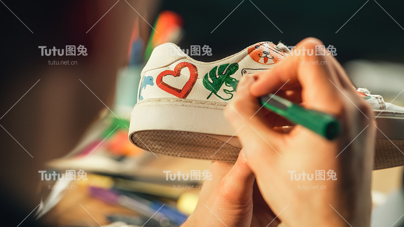 近距离艺术家的手，拿着马克笔和绘画设计的鞋子。画家创造定制运动鞋，使自己的产品。千禧一代和创业公司的概念。