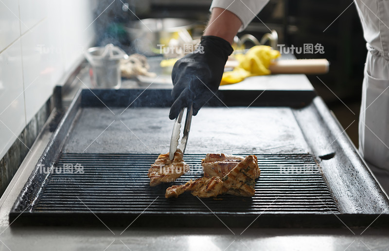 在烤架上烹饪鸡肉。厨师在餐厅的厨房里用夹子转动家禽片