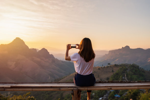 年轻的女人旅行者在日落时用智能手机拍照的山