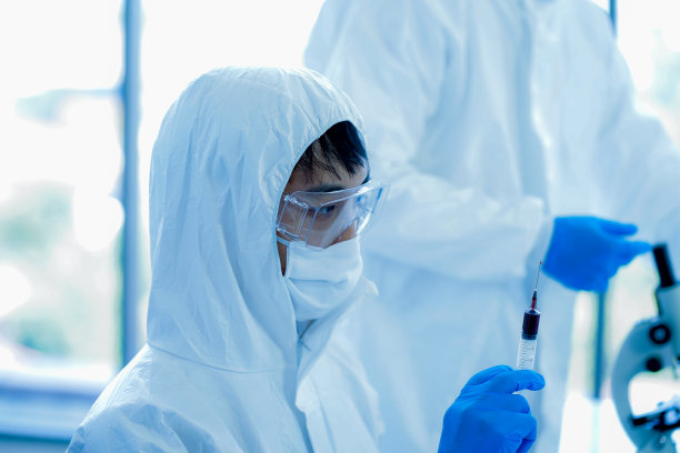 年轻的亚洲男性医学科学家穿着防护服、眼镜、面罩和连身衣，在临床实验室做试验样本