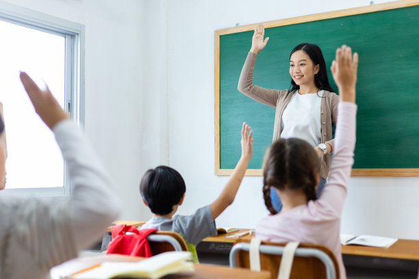 多样化的小学生在课堂上举手回答老师的问题。返校理念