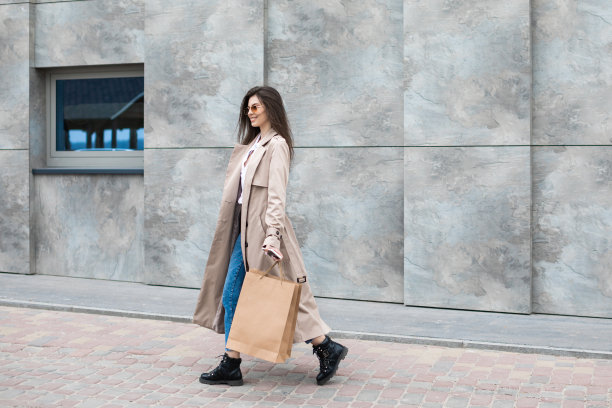 一个女孩穿着休闲的衣服，购物袋和购物中心附近，微笑着把她的包，消费主义销售和人的概念