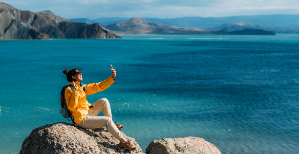 一名女旅行者正在大海的背景下进行视频通话。一名旅行者以大海为背景，用智能手机自拍。在海滨的旅行者。