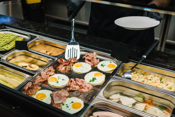 男服务员或女服务员把食物放在盘子里。自助早餐，家庭早午餐。人们在豪华餐厅的室内提供自助餐。餐饮和餐饮。庆祝晚会。