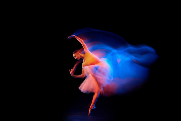 光与光辉之舞。美丽优雅的女孩，女芭蕾舞者跳舞孤立的黑色背景在混合霓虹灯。