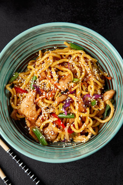 中国炒面，鸡肉和蔬菜在黑色混凝土背景的陶瓷碗。现代构图与亚洲食物-自制面条在中国风格。用芝麻炒乌冬面。